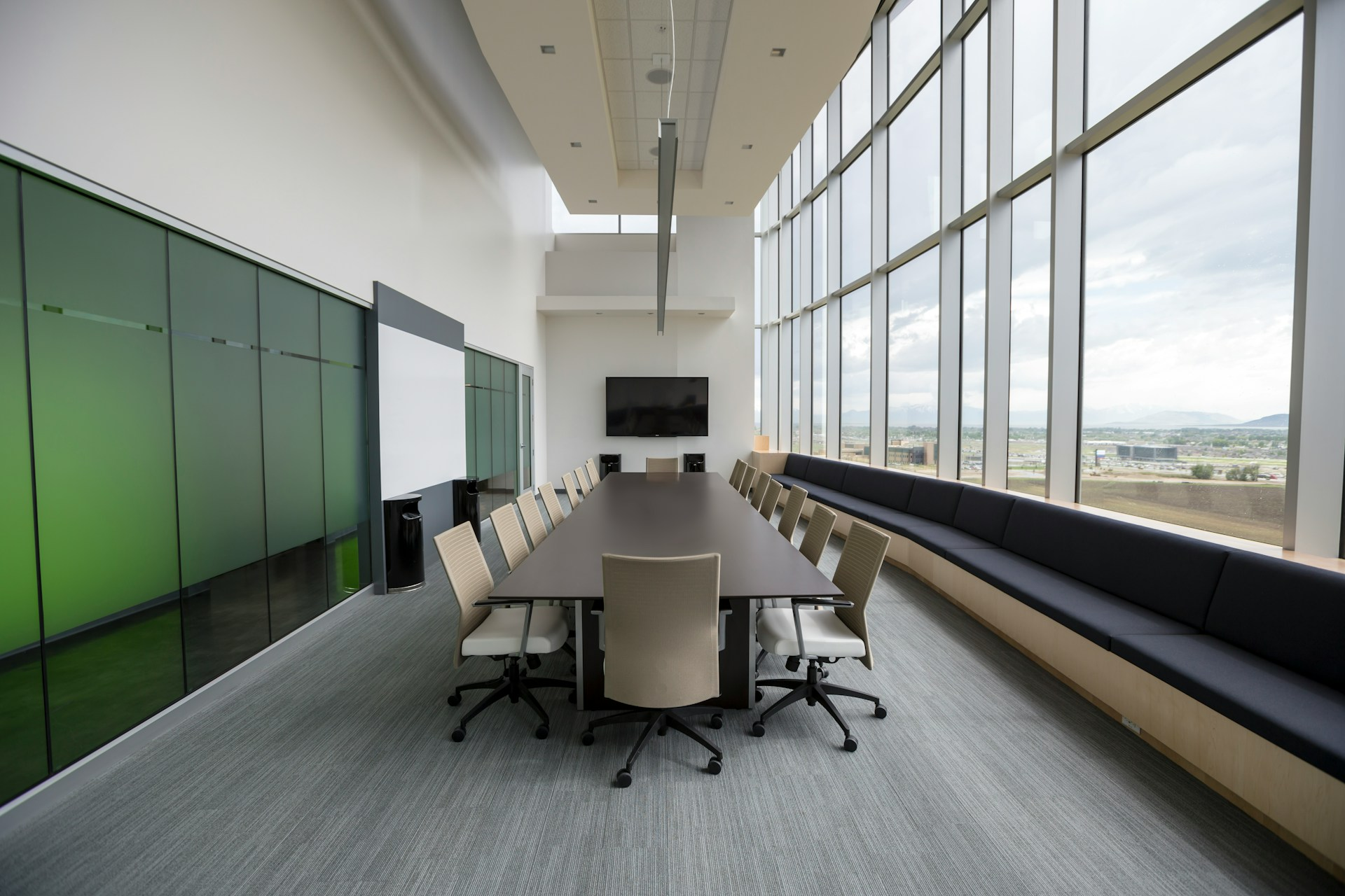 A modern conference room with a long table, office chairs, and large windows overlooking a scenic view, representing professional business solutions and repair services in Riga, Latvia. Services include office computer maintenance and conference room setup.